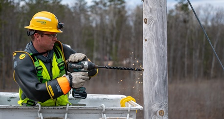 Lineworker drilling on an electric power pole